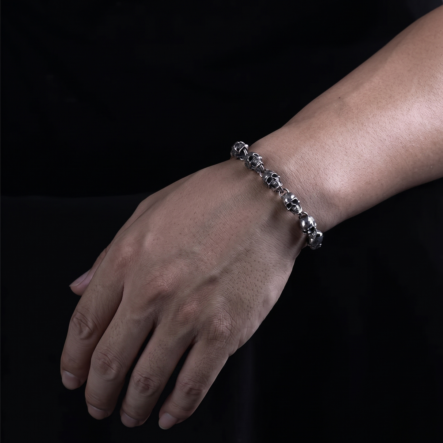 Hand wearing a silver bracelet on a black background