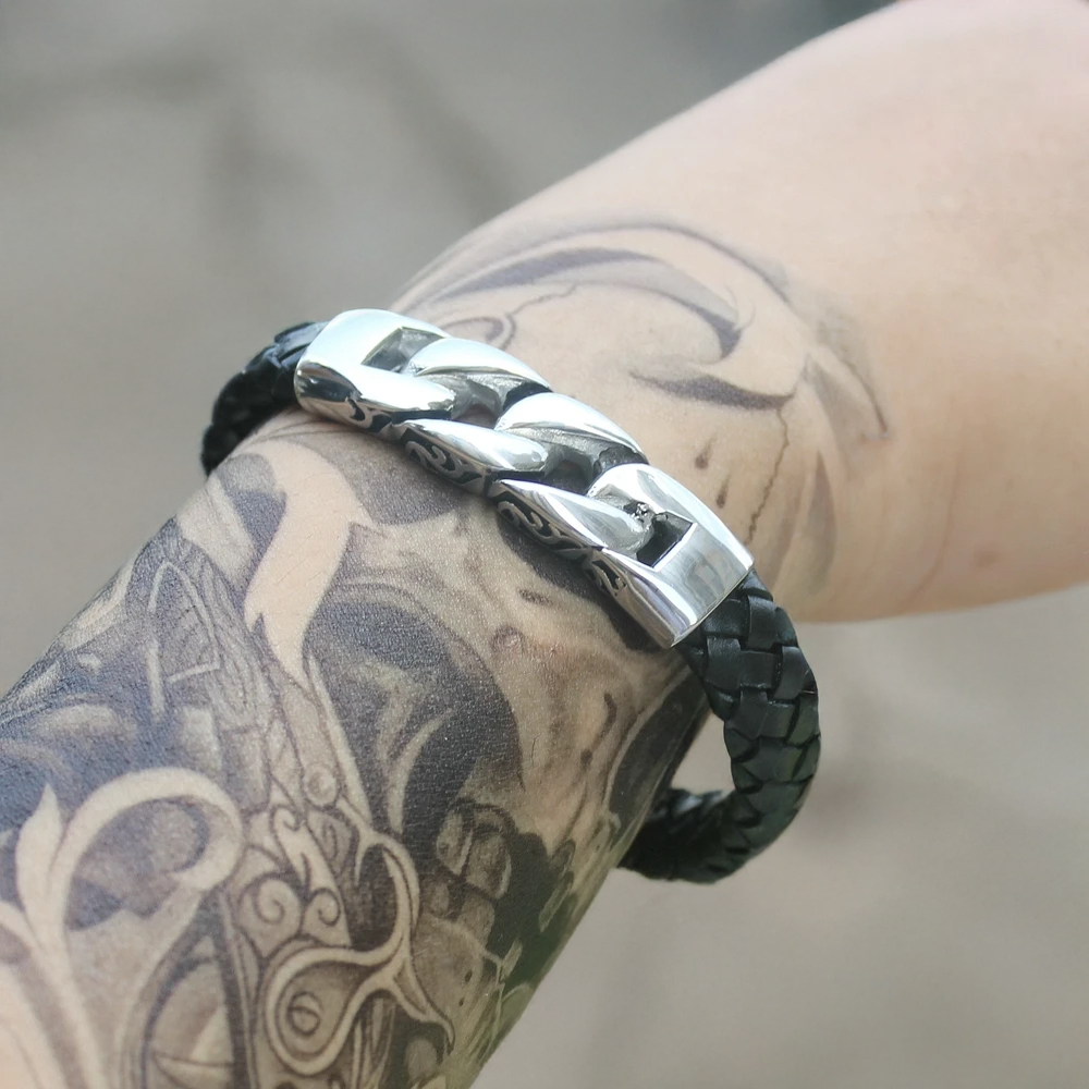 Black braided leather and silver metal bracelet on a tattooed arm.